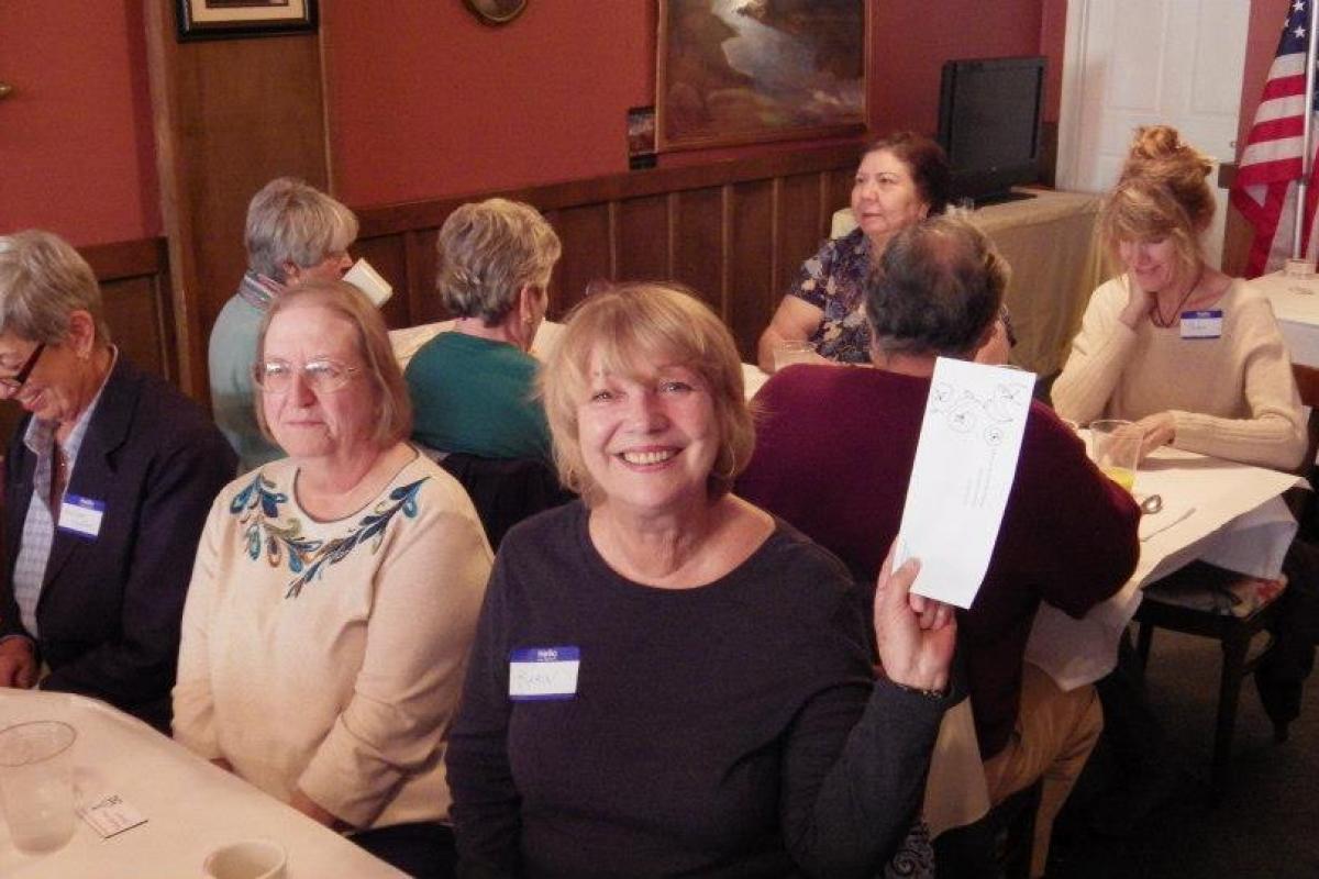 Volunteers sitting at table, smiling at camera - one holding up a card